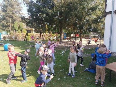 Dzieci biegają po trawie i łapią bańki